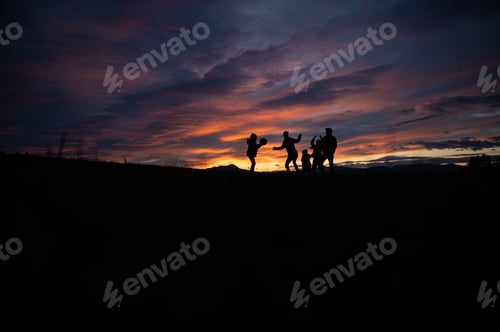 Preview: Silhouette of a family playing with a ball outside on a hill at sunset