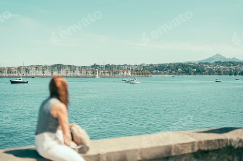 Preview: out-of-focus woman observing a bay with seafaring ships
