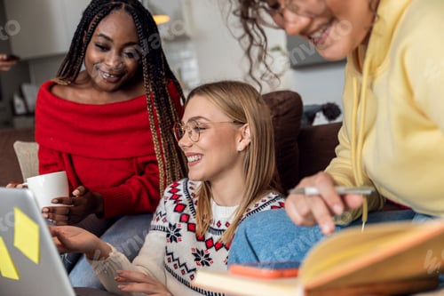 Preview: Diverse group female students learning at home using laptop and books.