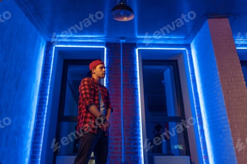 Preview: Young hipster man in stylish cap and checked shirt standing near the wall