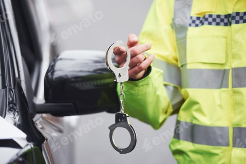 Preview: Male police officer in green uniformstanding with handcuffs near automobile