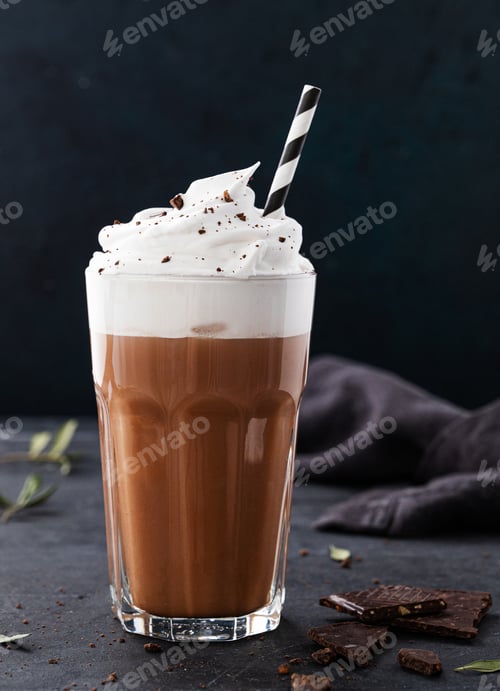 Preview: Hot chocolate with whipped cream and chocolate pieces in a tall glass on a dark background