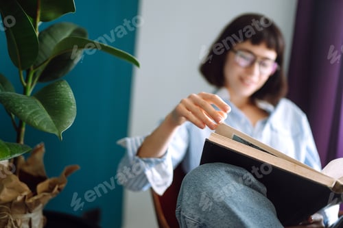 Preview: A young woman reads a book at home, sitting in her living room. Concept of rest, relaxation.