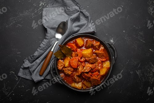 Preview: Beef meat stew with potatoes, carrot and delicious gravy in black casserole pot with bay leaves