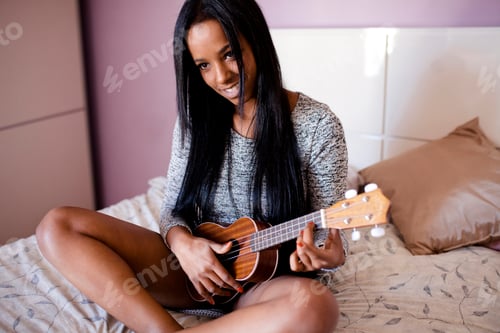 Preview: Multiracial woman plays ukulele lying over bed