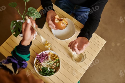 Preview: cropped shot of man and woman eating vegan tofu burger and salad bowl in vegan cafe, vegetarian