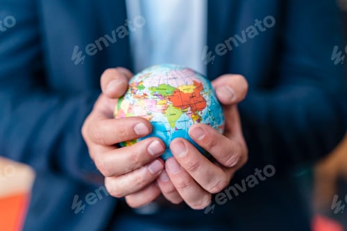 Preview: Close-up of businessman holding miniature globe in office