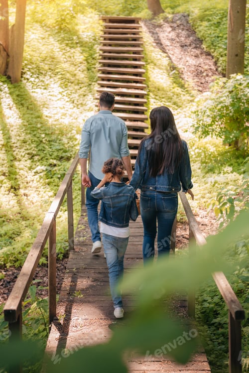 Preview: back view of young family walking in sunny forest