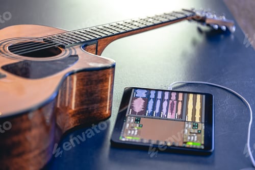 Preview: Acoustic guitar and tablet on the table, music recording concept.