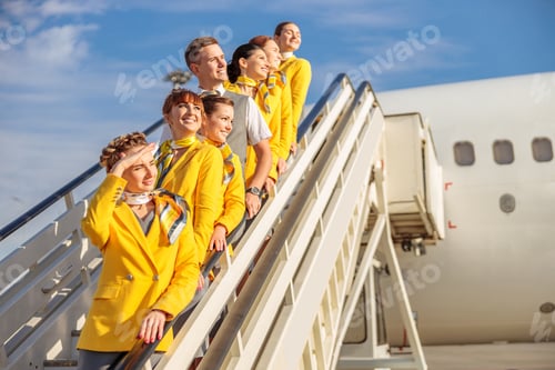 Preview: Cheerful airline workers standing on airplane stairs under blue sky