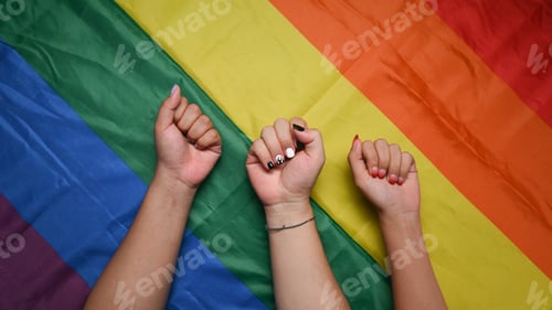 Preview: Diverse people making power fist gesture on pride LGBT rainbow flag.