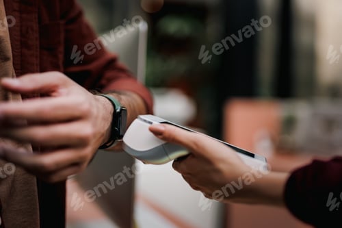 Preview: Businessman standing in front of a reception, paying for his cost with a smart watch.
