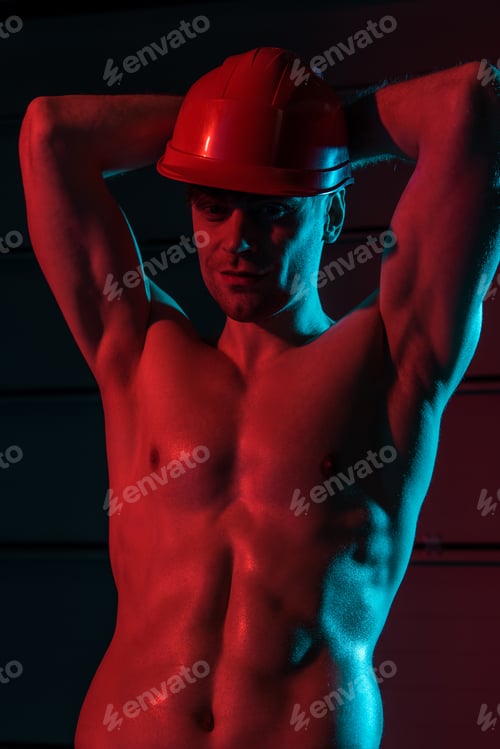 Preview: sexy shirtless fireman in protective helmet posing with hands up in darkness