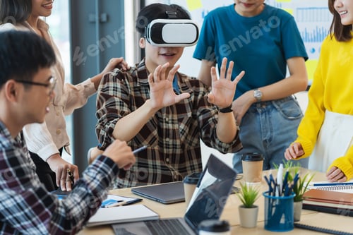 Preview: Group of young Asian business people using virtual reality glasses during meeting testing virtual
