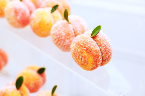 Preview: Delightful peach-shaped treats with vibrant colors and green leaves on display at a dessert stall