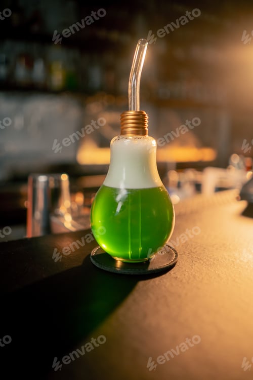 Preview: close up on the bar counter green cocktail in a light-bulb-shaped glass is drunk through a straw