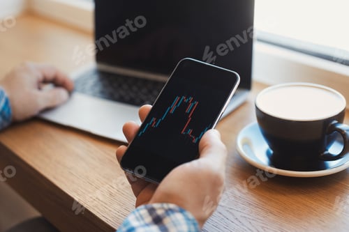 Preview: Man trader holding smartphone in hands with financial charts and trading online investment data