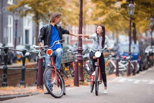 Preview: Young happy caucasian couple on bikes in old streets in Amsterdam