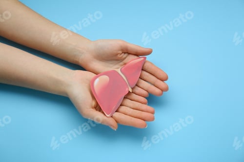 Preview: Woman holding paper liver on light blue background, closeup and top view. Hepatitis treatment