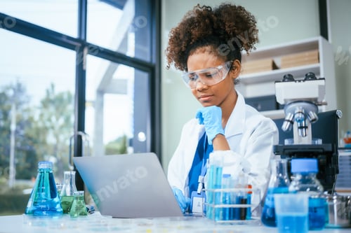 Preview: An African American female scientist in a white coat and blue gloves smiles confidently, holding