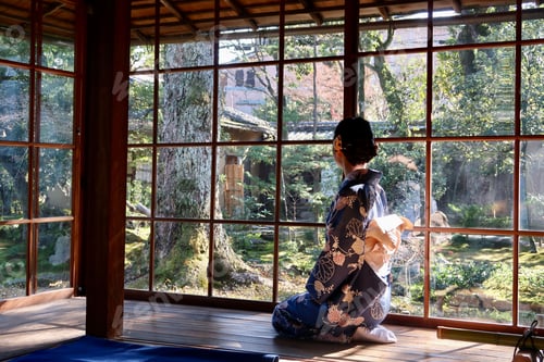 Preview: Young woman wearing a traditional Japanese kimono sitting at a window, looking out at a lush garden