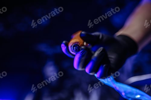 Preview: Tattoo machine in the hands of a tattoo artist. Dark studio with blue light.