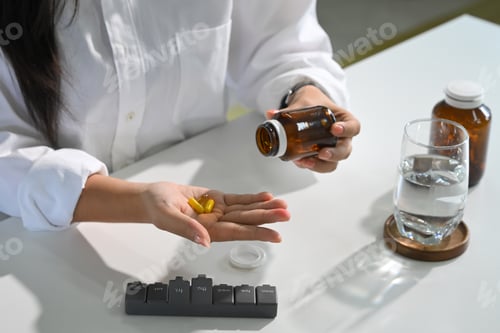 Preview: Woman taking dietary supplements with water and a weekly pill organizer on the table.