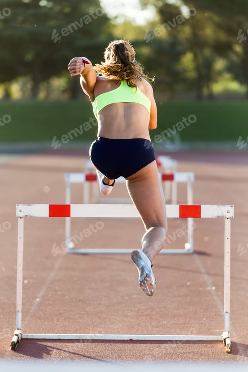 Preview: Young athlete jumping over a hurdle during training on race trac
