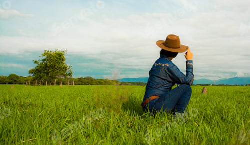 Preview: woman with jeans and a brown hat sitting on grasses and admiring with the view