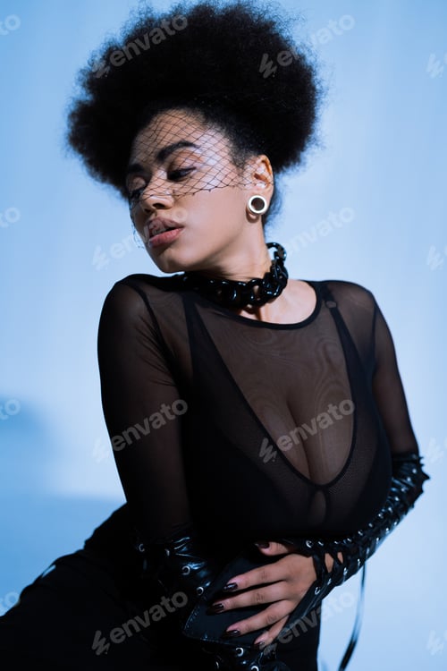 Preview: young african american woman in sexy outfit and black veil posing on blue