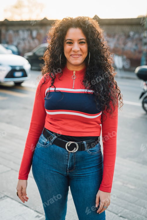 Preview: Mid adult woman with long curly hair on city sidewalk, portrait