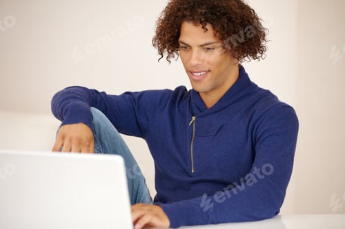 Preview: Handsome young ethnic man working on his laptop on his couch