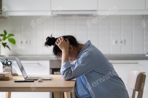 Preview: Stressed frustrated female freelancer sitting in front of laptop at home feeling unmotivated