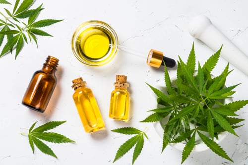 Preview: Cannabis oil in glass bottles and cannabis leaves at white table.