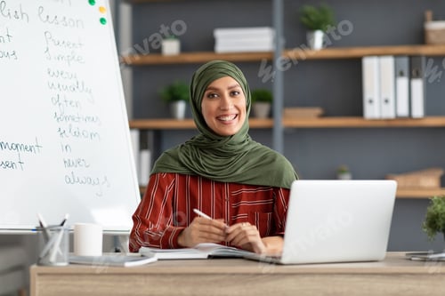 Preview: Islamic teacher in headscarf sitting at desk looking at camera