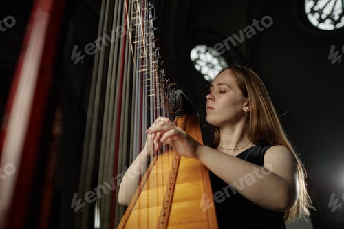 Preview: Portrait of Female Musician Playing Harp with Passion in Dim Light in Church