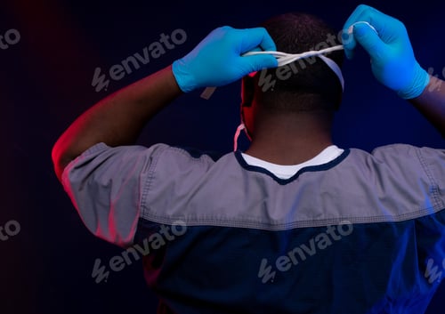 Preview: Doctor putting on mask wearing blue gloves in scrubs