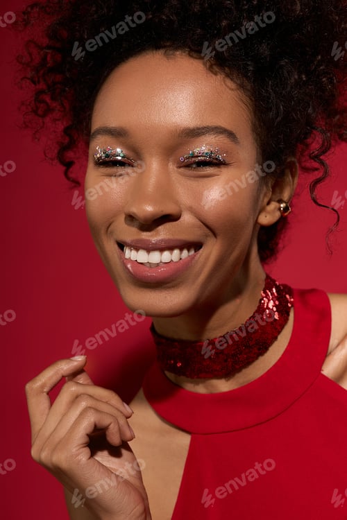 Preview: Young woman with sparkling makeup radiates joy and confidence in a vibrant red setting