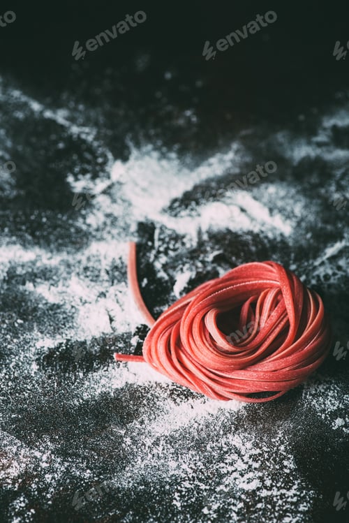 Preview: close up view of red raw tagliatelle pasta on table covered by flour