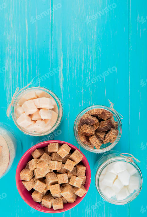 Preview: top view of different types of sugar in glass jars on blue wooden background with copy space