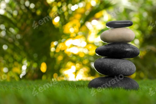 Preview: Stack of stones on green grass against blurred background, space for text. Zen concept