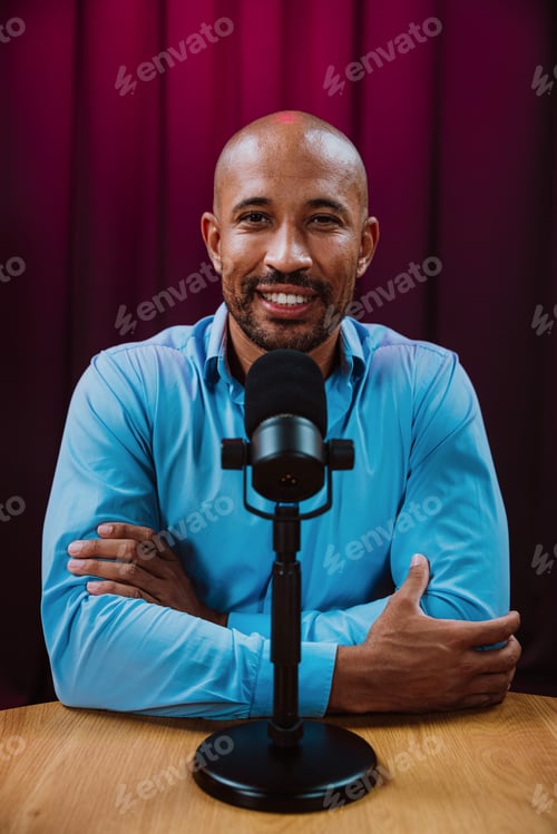 Preview: Smiling man speaking into a professional microphone while recording a podcast