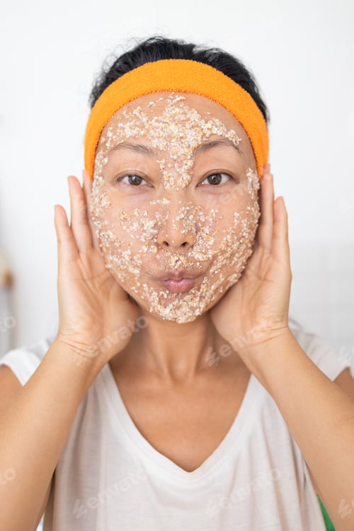 Preview: Portrait of a happy Asian woman using natural secrets for skin care (ingredients on the table: oats,