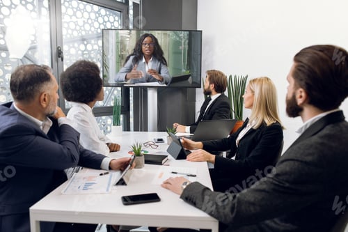 Preview: Team of diverse business people looking at screen during video conference in office, listening young