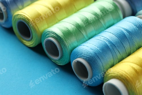 Preview: Different spools of sewing threads on light blue background, closeup