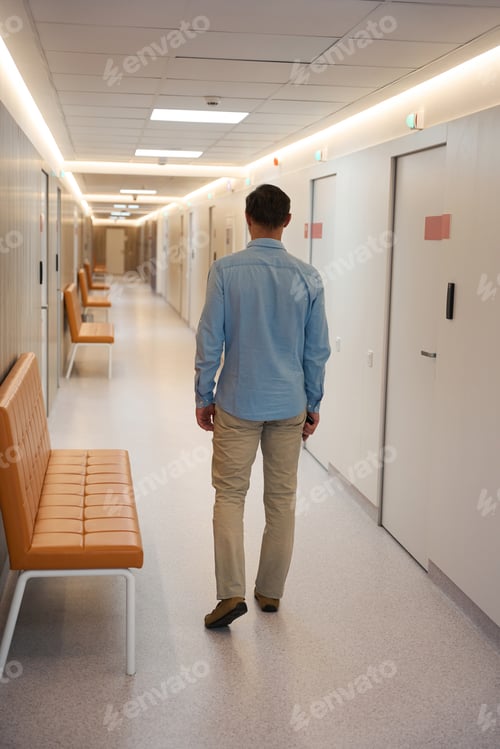 Preview: Man standing in hallway with sofas along wall. Back view