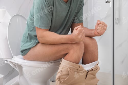 Preview: Man suffering from hemorrhoid on toilet bowl in rest room, closeup