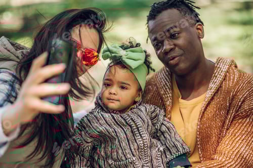 Preview: Multiracial family of three taking selfie with a smartphone in the park