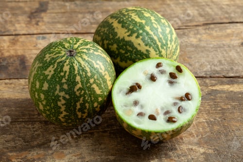 Preview: Whole and halved red seeded citron melon on wooden background close up