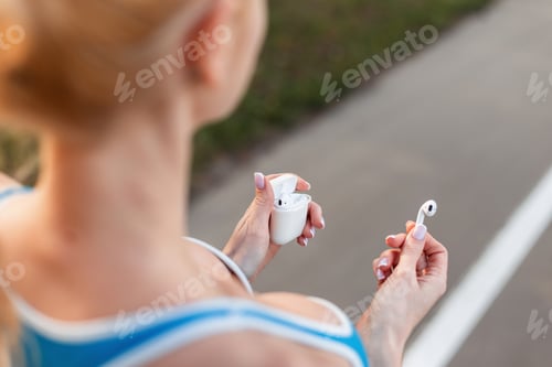 Preview: Young woman is holds case with wireless modern headphone outdoors. Close-up. Woman workout and run